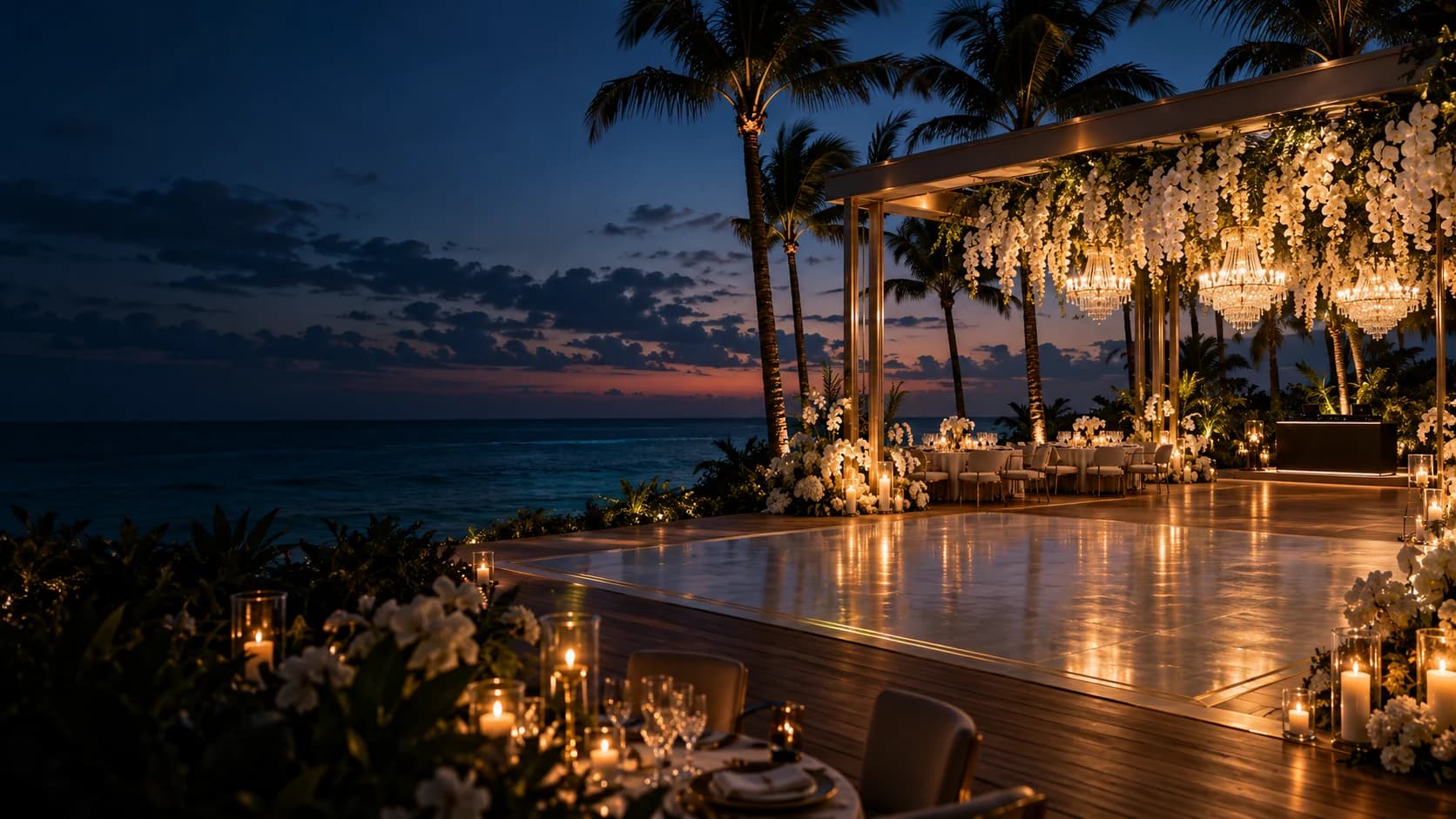 An elegant oceanfront reception setting with white florals and warm chandelier lighting